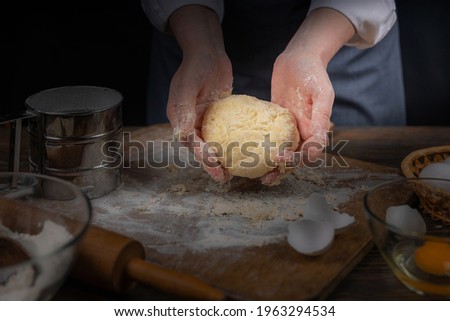 Women's hands, flour and dough. A woman, in an apron cooking dough for homemade baking, a rustic home cozy atmosphere, a dark background with unusual lighting.