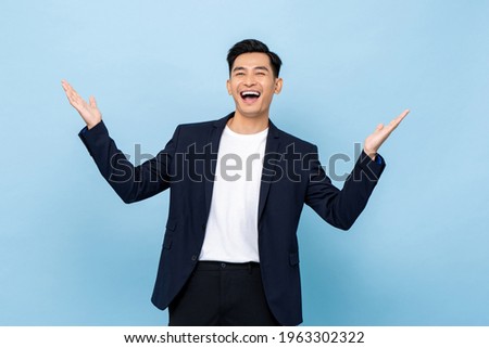 Surprised worry free handsome Asian man in semi formal clothes smiling and opening hands in light blue isolated studio background Royalty-Free Stock Photo #1963302322