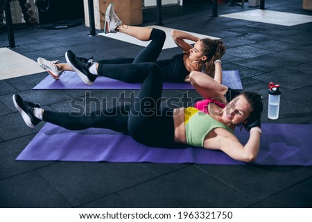 Serious lady and her personal trainer working their abdominal muscles Royalty-Free Stock Photo #1963321750