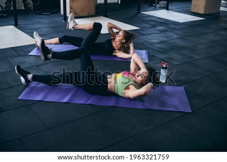 Fitness trainer and her client strengthening their upper abdominal muscles Royalty-Free Stock Photo #1963321759