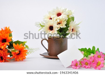 Plastic flowers on tea cup with refill paper on white background. Minimal style, romantic mood.