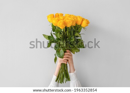 Female hands with beautiful yellow roses on light background