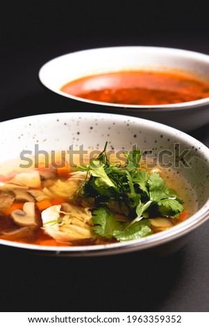 Chicken soup with vegetables amd mushrooms, fresh parsley and dill on top. Served in a white bowl over black background. Healthy eating, delicious dinner idea.