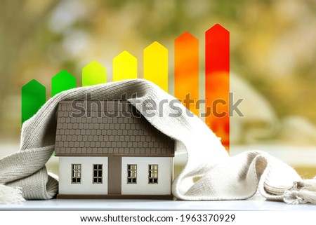 Figure of house with scarf and energy efficiency rating outdoors. Concept of winter heating Royalty-Free Stock Photo #1963370929
