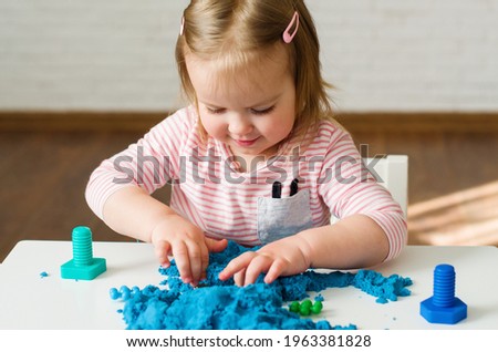 Little girl playing with blue kinetic sand. Educational games with children for fine motor skills. Sand therapy indoors. Concept of sensory and creativity game, therapy hand, development of fine motor Royalty-Free Stock Photo #1963381828