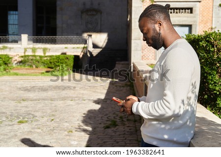 Handsome african american guy chatting via smartphone standing, cheerful dark-skinned man enjoying free time blogging in networks via smartphone. High quality photo
