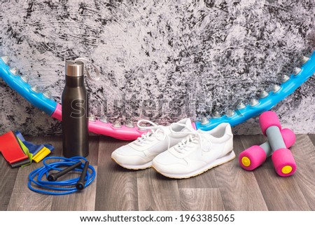 training equipment at home - white sneakers and dumbbells, jump rope and rubber bands, hoop and water bottle for training, texture background