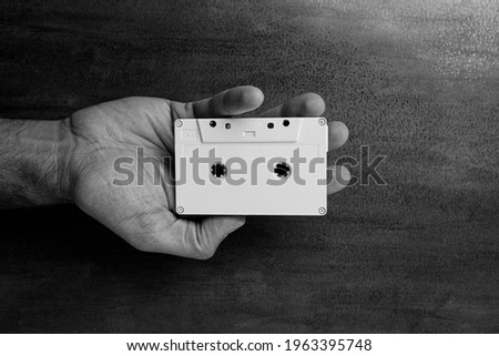 There is a white audio magnetic cassette in the man's hand. Below is a wooden background. Black and white