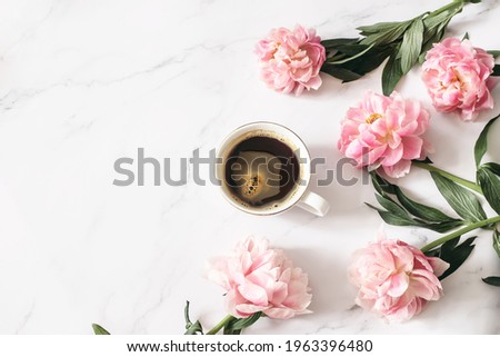 Feminine floral composition. Cup of coffee and pink peonies flowers on white marble table background. Empty space. Flat lay, top view. Picture for blog. Spring breakfast concept. Styled stock photo. 