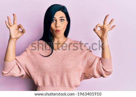 Young caucasian woman wearing casual clothes looking surprised and shocked doing ok approval symbol with fingers. crazy expression 