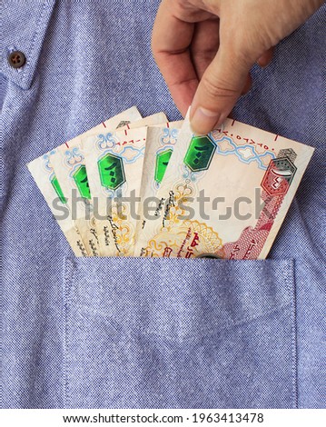 Hand pulling out one hundred dirhams from the pocket of a blue color shirt. Closeup, paper money. United Arab Emirates (UAE) currency.