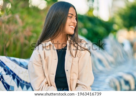 Young hispanic girl smiling happy sitting on the bench at the park.