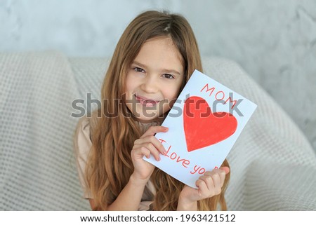 Girl holding greeting card for Mom on Mothers Day with inscription Mom, I love you. Daughter prepared homemade gift painted postcard with red heart. Saint Valentine, birthday. Happy childhood concept