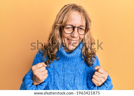 Middle age blonde woman wearing glasses and casual winter sweater excited for success with arms raised and eyes closed celebrating victory smiling. winner concept. 