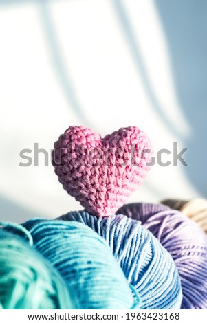  Women's hobby. Crochet and knitting.  Multicolored skeins  and pink knitted heart on a white background. Shadows. Valentine's day. Verticale