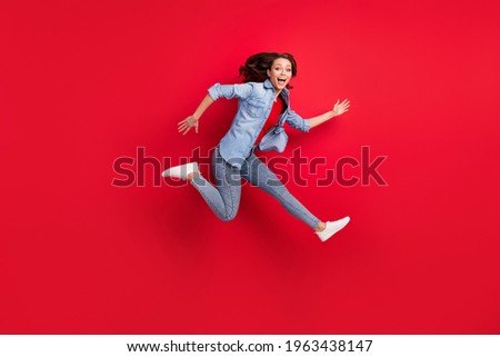Photo of adorable excited young woman wear jeans shirt smiling jumping high hurrying isolated red color background Royalty-Free Stock Photo #1963438147