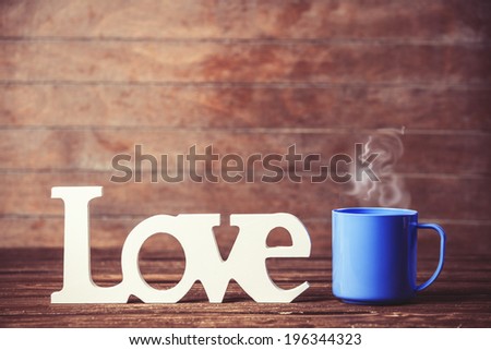 Tea or coffee cup with word Love on wooden table.
