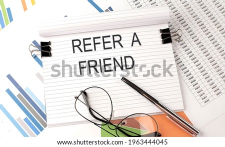 Notebook with text REFER A FRIEND on the table with charts,pen and glasses.