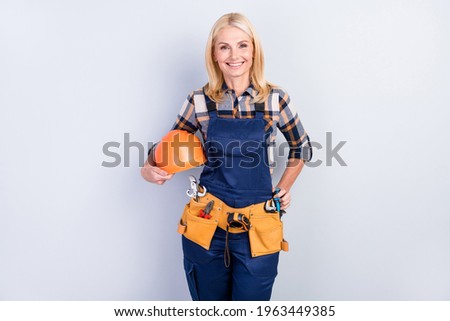 Photo of cheerful petty mature handywoman workwear smiling holding hardhat isolated grey color background Royalty-Free Stock Photo #1963449385