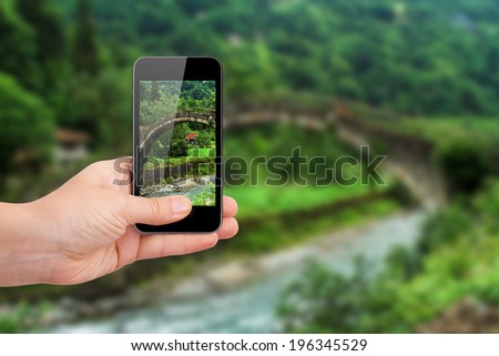 Hand holding smart phone focused on green landscape of plateau on blurry background.