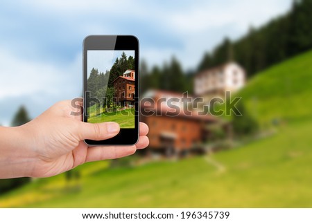 Hand holding smart phone focused on green landscape of Ayder Plateau in Rize, Turkey on blurry background.