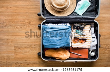  Top view of Luggage,suitcase bag with clothing and mask on wood floor.summer and vacation with coronavirus pandemic.copy space Royalty-Free Stock Photo #1963461175