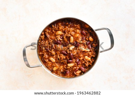 Close up view of cowboy beans with ground beef, jalapeno pepper and bacon in cooking pan over light stone background. Top view, flat lay