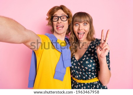 Portrait of funny handsome guy attractive lady make selfie show v-sign tongue out isolated on pink color background