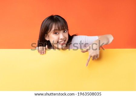 Young Asian girl pointing her finger down on yellow and orange background Royalty-Free Stock Photo #1963508035