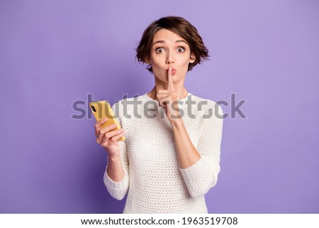 Photo portrait of girl with bob hair keeping secret finger near lips using app isolated on pastel violet color background
