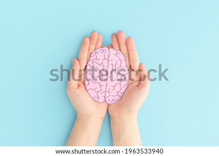 Woman hands holding human brain shape made from paper on light blue background. Awareness of Alzheimer, Parkinson's disease, dementia, stroke, seizure or mental health. Neurology and Psychology care. Royalty-Free Stock Photo #1963533940