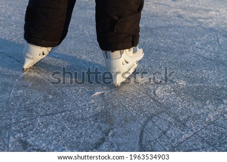 A child in white skates clumsily rides in winter on the ice of a river or lake.