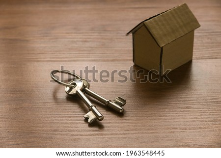 Concept of property or real estate with a cardboard house and key on wooden table.