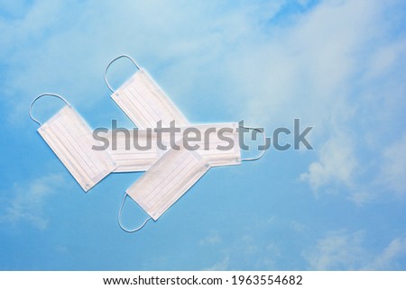 Airplane model made of protective masks on a bright blue sky with clouds. Safe travel by plane concept.