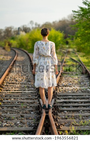 Young and beautiful Caucasian girl walking on a railway that splits in two directions, concept about choosing a direction in life, weighing the decision to follow a certain path to the future. Royalty-Free Stock Photo #1963556821
