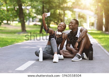 Joyful Sporty African Couple Taking Selfie On Smartphone After Training In Park, Posing For Photo On Path Outdoors. Free Space