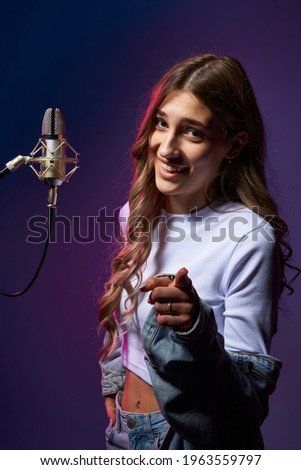 Girl blogger recording audio podcast. Happy smiling girl with microphone pointing at camera at you