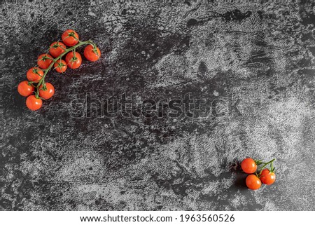 Flat lay moody dark food photography of fresh cherry tomatoes with copy space. Top view image with a vintage look and a black stone background.