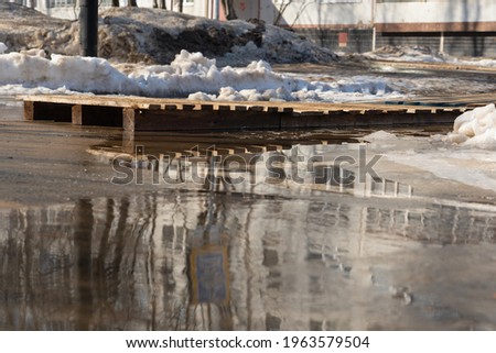 A wooden pallet bridge over a puddle on the asphalt. Russia in the spring.