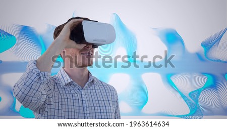 Composition of smiling man wearing vr headset over blue light trails. global connection, virtual reality and technology concept digitally generated image.