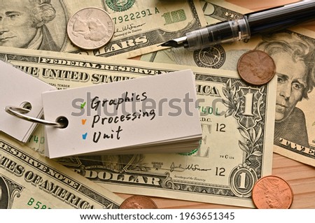 On top of the dollar bills on the table, there is a word book with the financial term Graphics Processing Unit written on it.