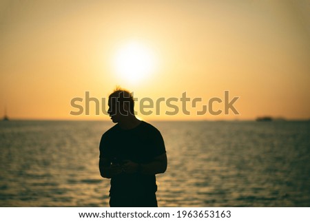 Silhouette medium shot Asian man standing on the beach with the sea and sky sunset background on the sunset time. Travel and relax concept. picture looking feeling Alone or sad.