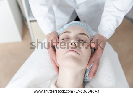 Young pretty girl lies on couch in beauty parlor and receives facial massage procedure. High quality photo