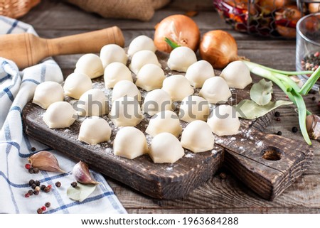 Homemade dumplings with meat on rustic wooden board and table with flour, horizontal