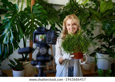 Joyful female blogger with houseplants recording a video