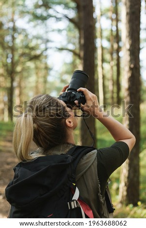 Young woman hiker with taking photos with a modern mirrorless camera in green forest.