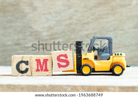 Toy forklift hold letter block S to complete word CMS (Abbreviation of Content management system) on wood background