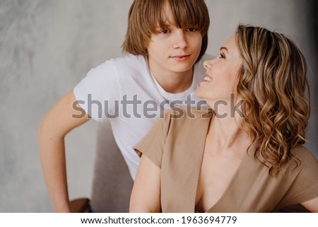 A mother and son in beige and white clothes pose for a photo shoot in the studio. happy single mother. memorabilia for the family. relationship between teenage children and parents. 