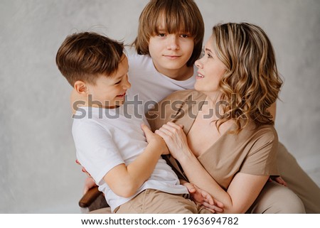 A mother and her two sons in beige and white clothes pose for a photo shoot in the studio. happy single mother. memorabilia for the family. relationship between teenage children and parents. 