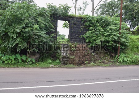Stock photo of old collapsed wall constructed using black stone road side of Indian village area, picture captured during rainy season. focus on foreground.